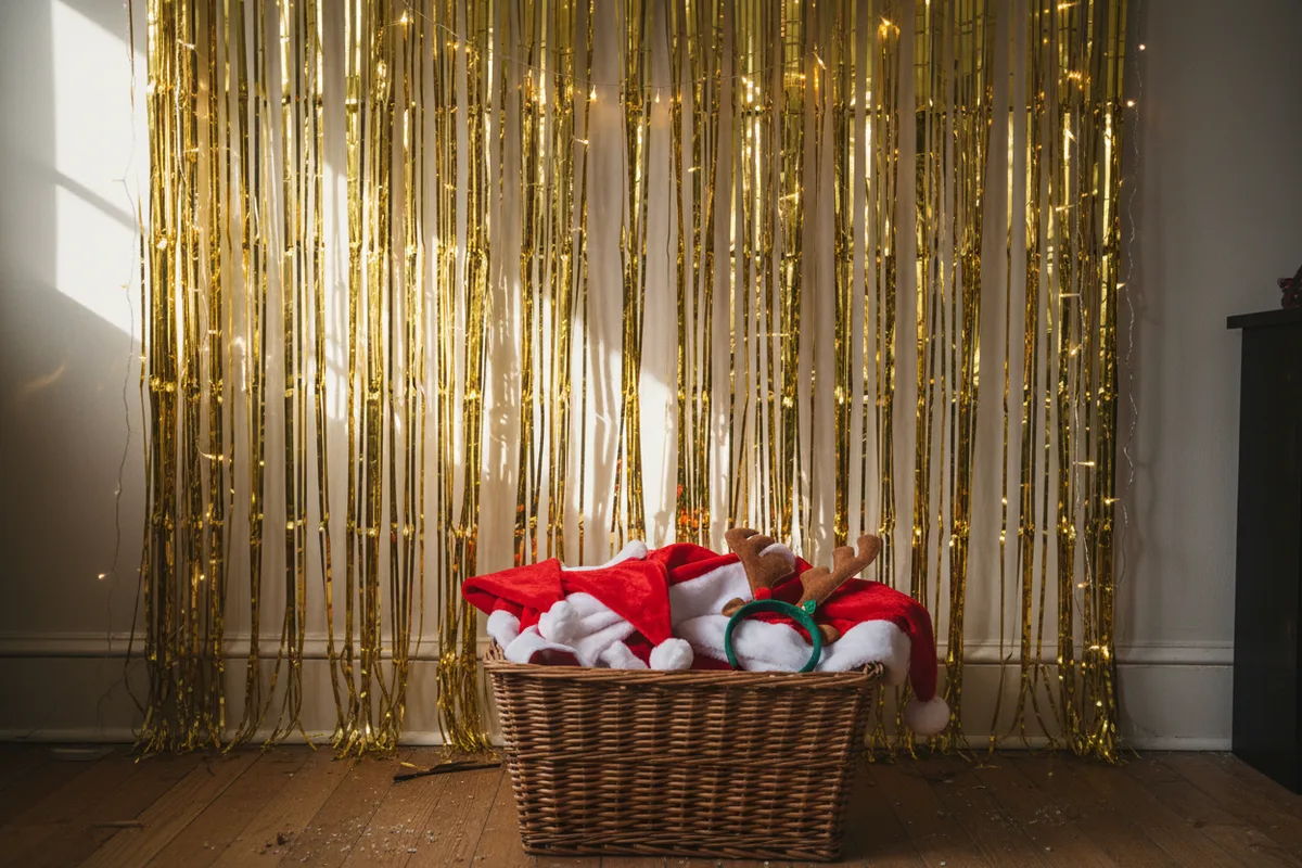 A holiday photo booth backdrop with fairy lights and a basket of props.